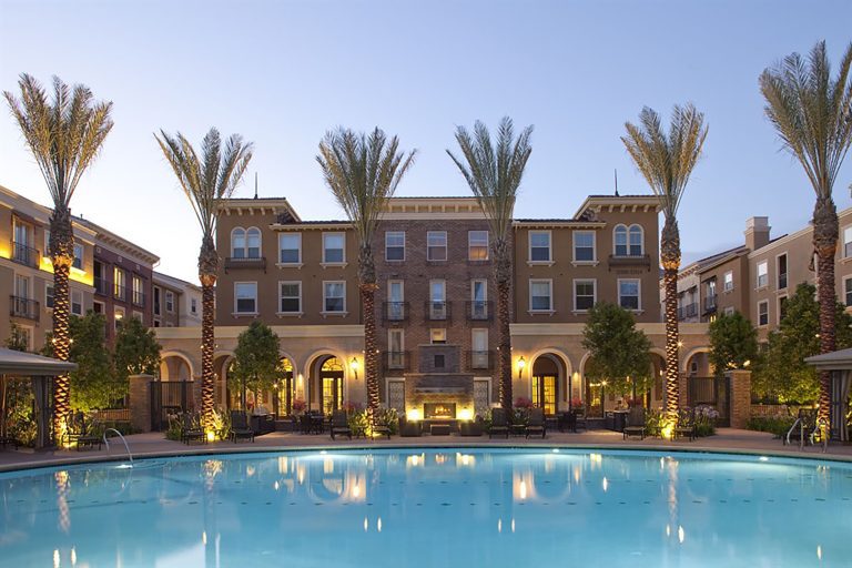Elegant apartment complex with palm trees, pool, and warm evening lighting.