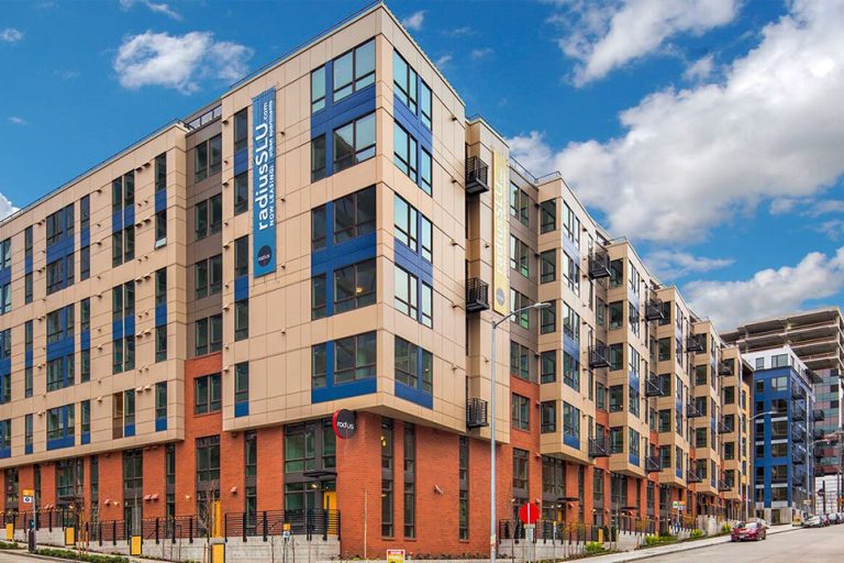 A modern multi-story apartment building with a mix of brick and panel facade under a blue sky.