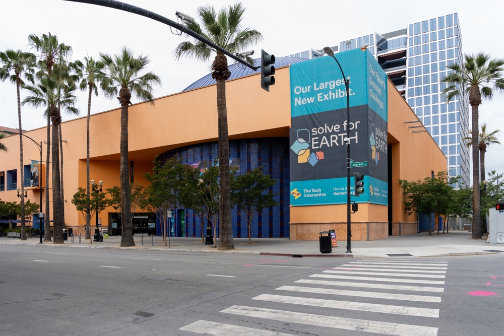 The Tech Interactive museum in San Jose, California, featuring palm trees and a large exhibit banner.