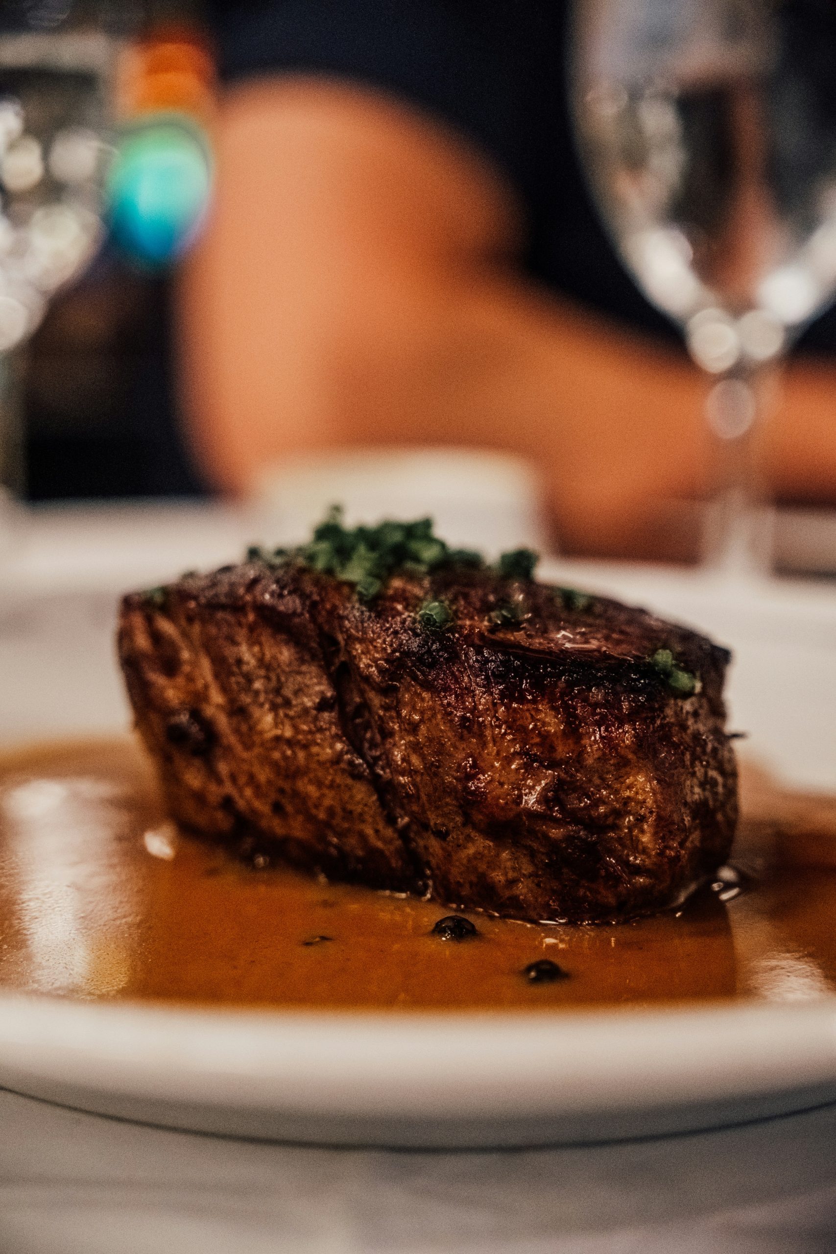 A seared steak topped with herbs, served in a rich brown sauce on a white plate.
