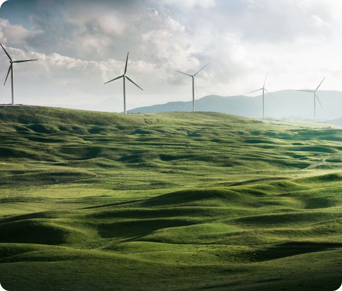 Wind turbines stand on rolling green hills under a cloudy sky, symbolizing renewable energy.