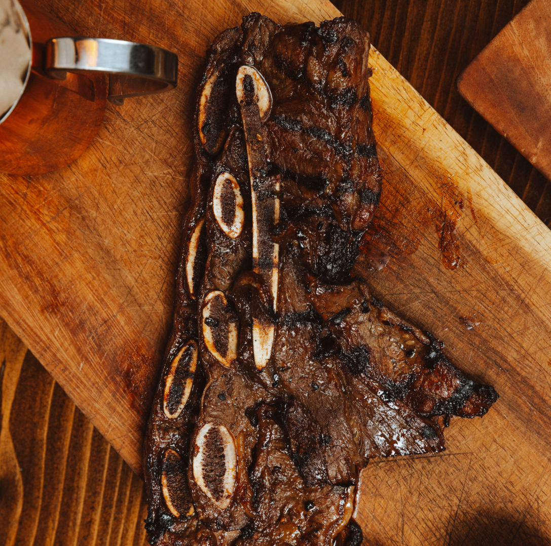 Grilled beef short ribs with visible bone segments on a wooden cutting board.