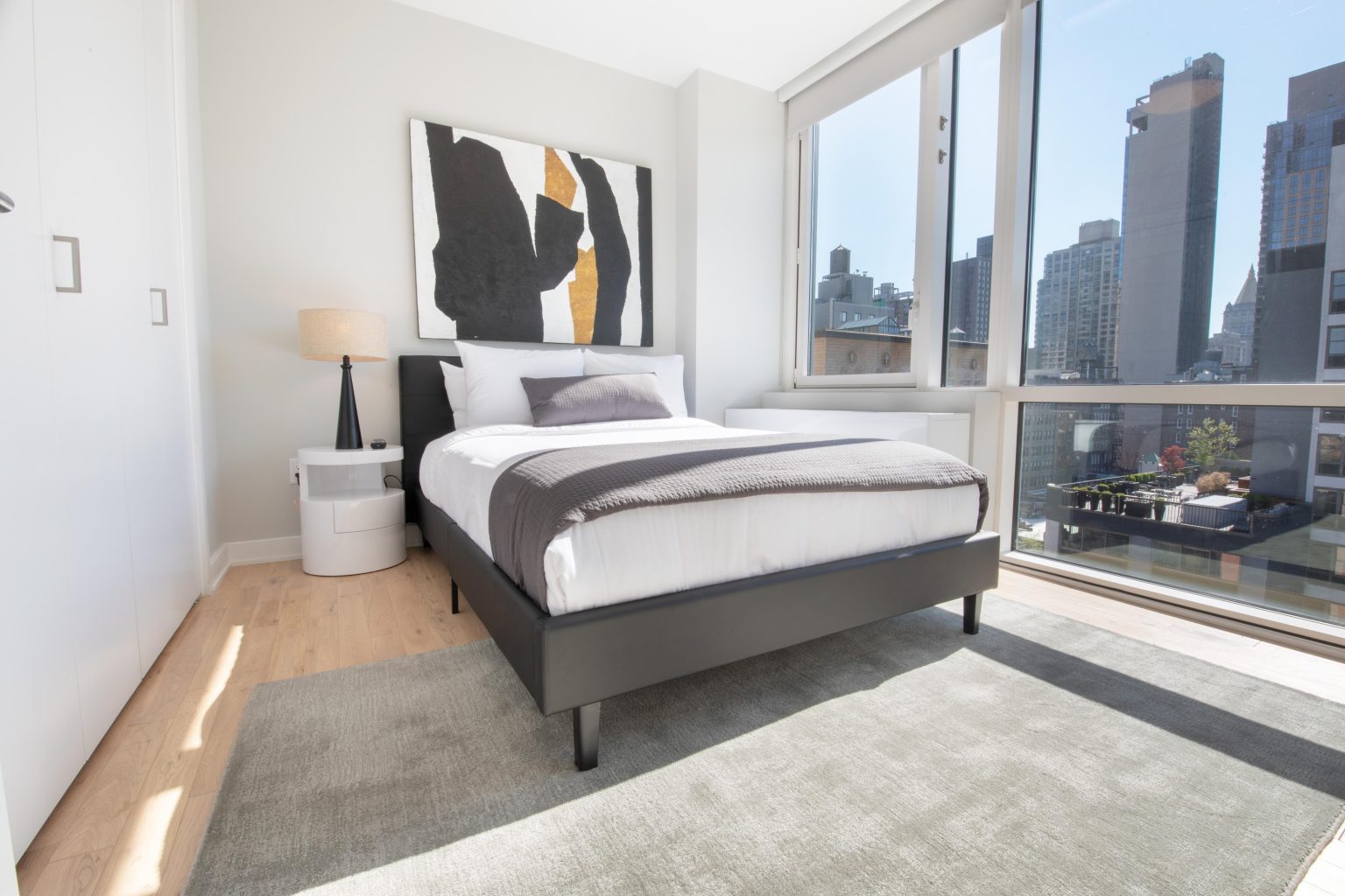 Modern bedroom with minimalist decor, large windows, and cityscape views.