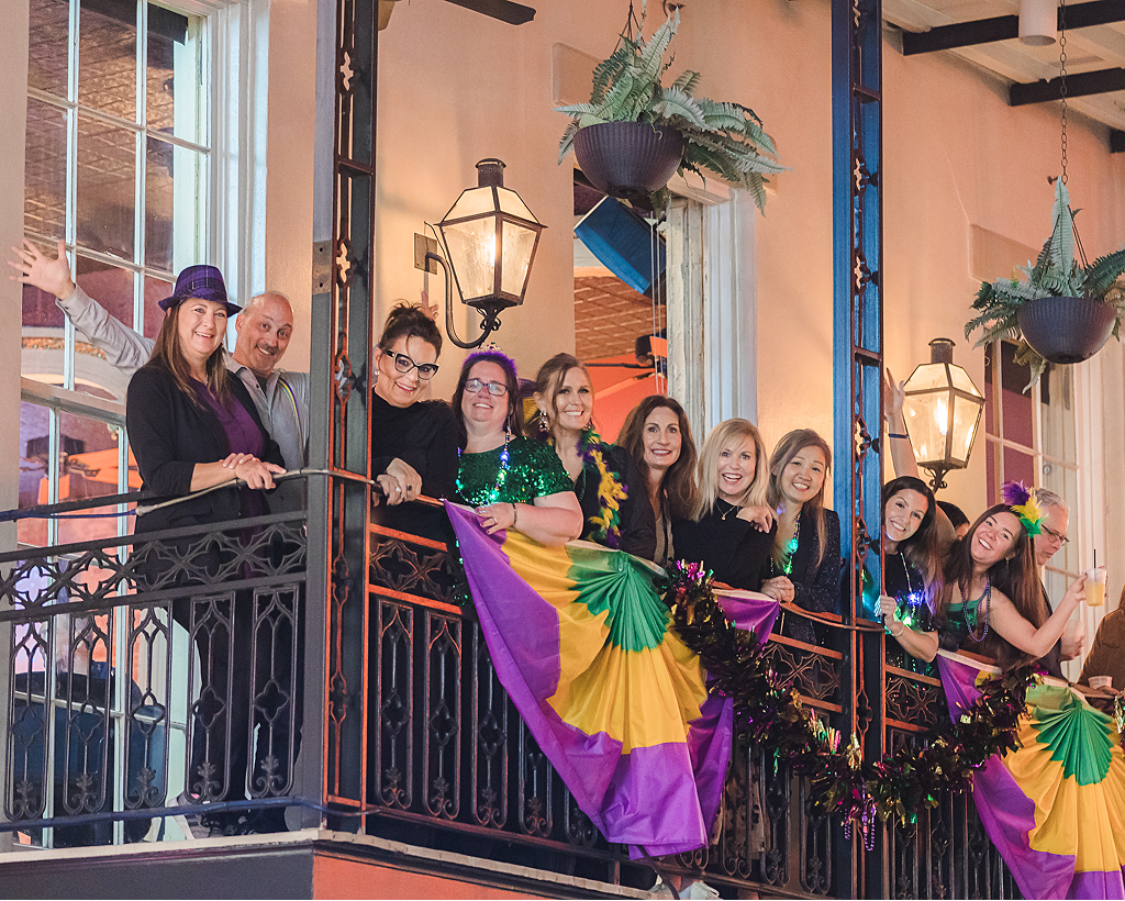 People celebrate on a decorated balcony with Mardi Gras colors and festive attire.