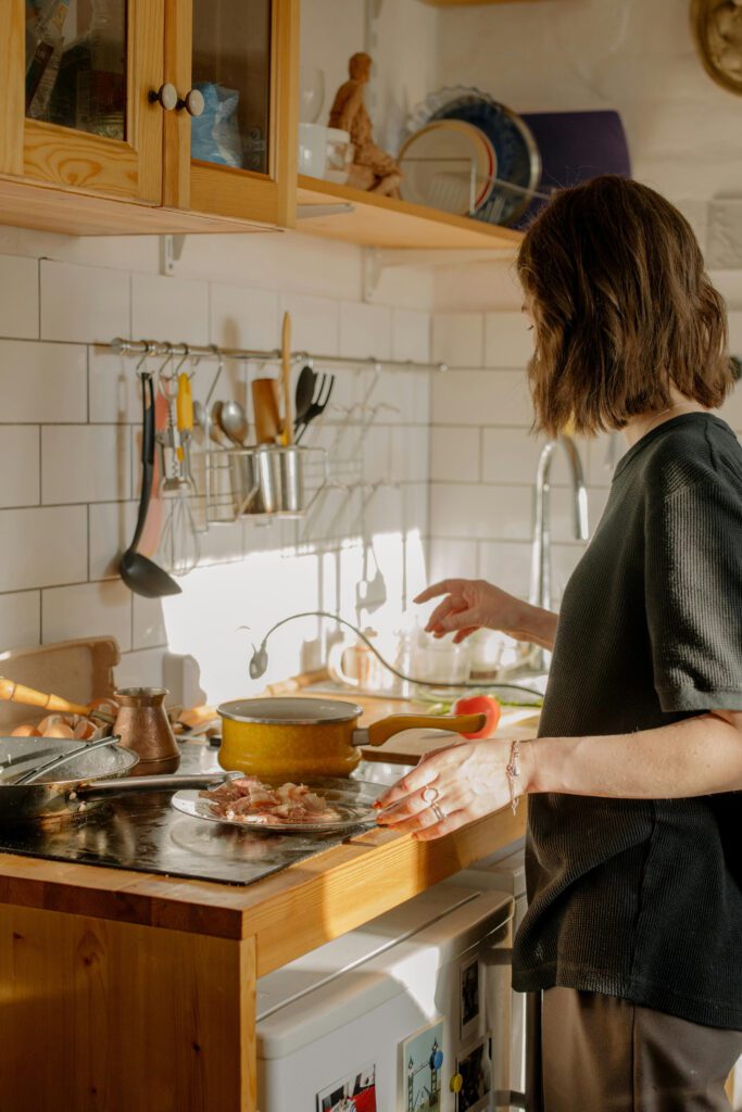 A woman prepares food in a cozy kitchen with wooden cabinets and white tiled walls.