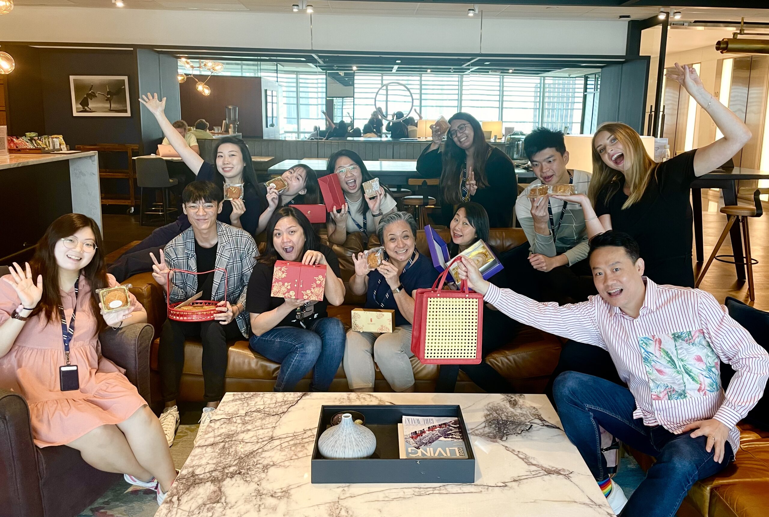 A group of people gathered indoors, holding festive items and posing cheerfully in a modern lounge.