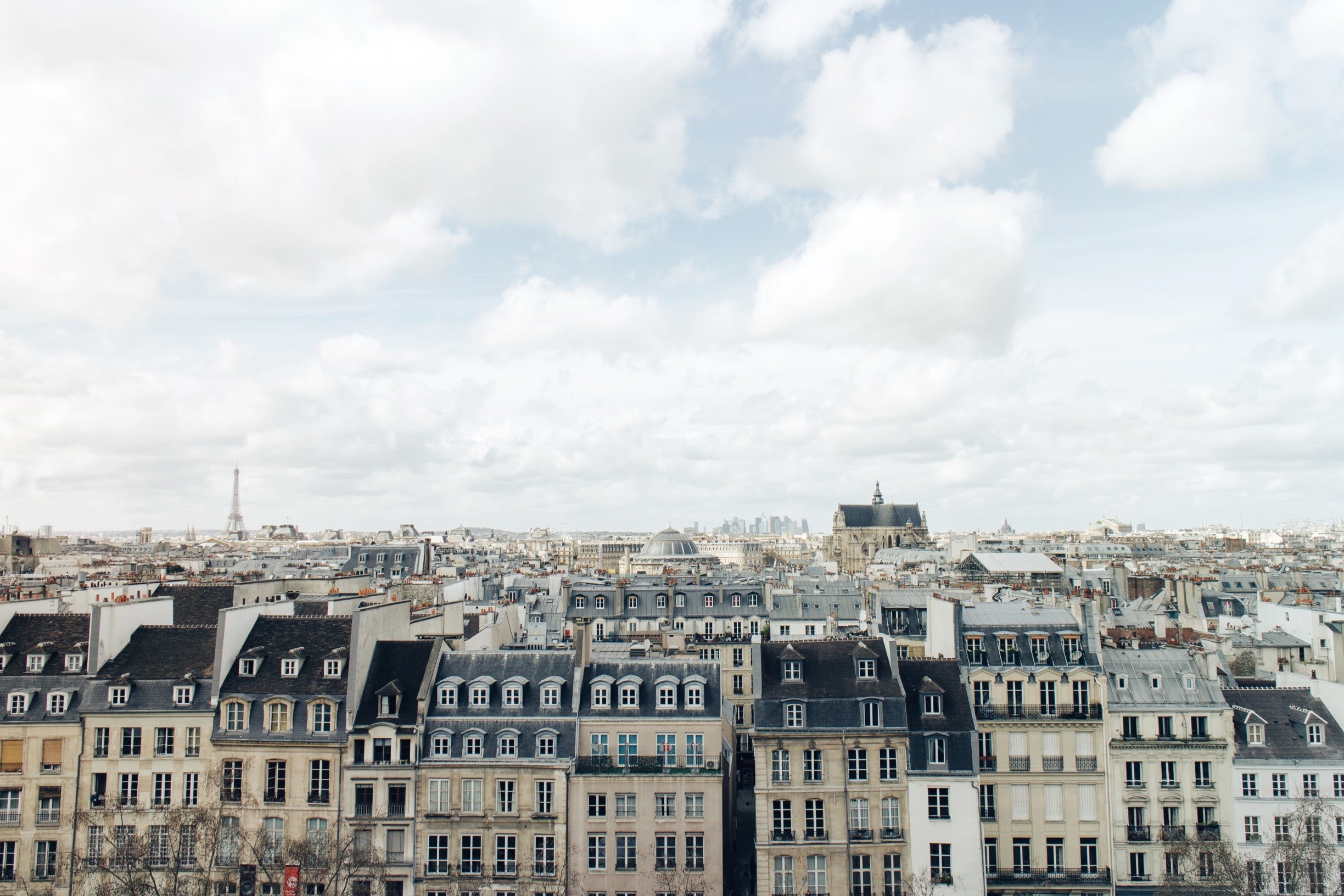 Parisian rooftops with the Eiffel Tower and La Défense visible under a cloudy sky.