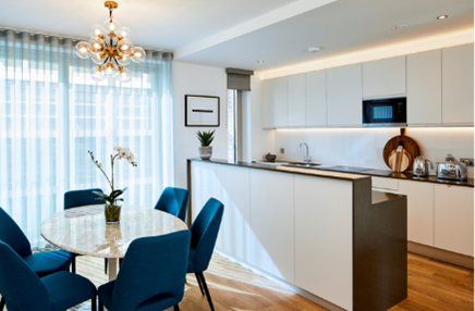 Modern open-plan kitchen and dining area with sleek white cabinetry and blue upholstered chairs.