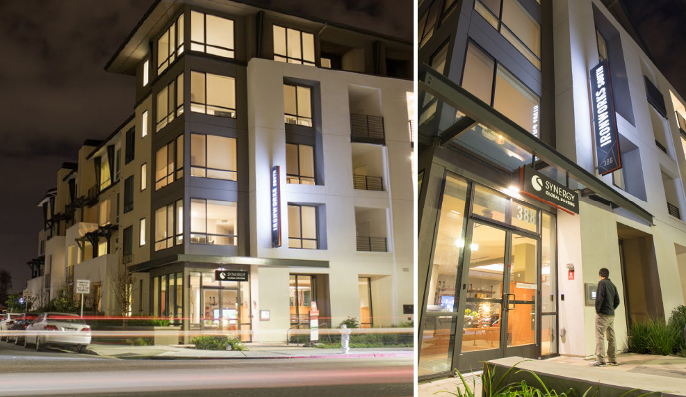 Modern multi-story building with large windows, illuminated signage, and a street-level entrance.