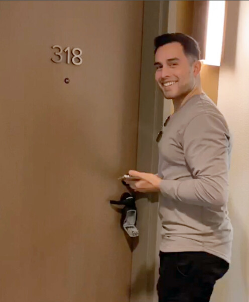 A person stands at door 318, holding a keycard near the handle in a hallway with warm lighting.