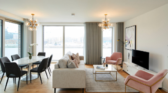 Modern living room with elegant decor, featuring pink chairs, a dining area, and large windows.