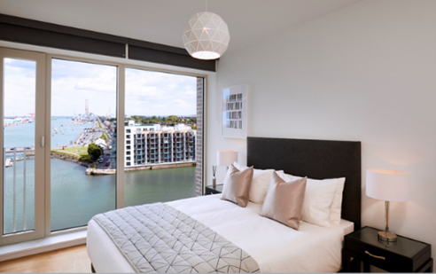 Modern bedroom with waterfront view, large windows, neutral decor, and geometric pendant light.