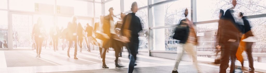 Blurred motion of people walking in a bright, modern indoor space with large windows.