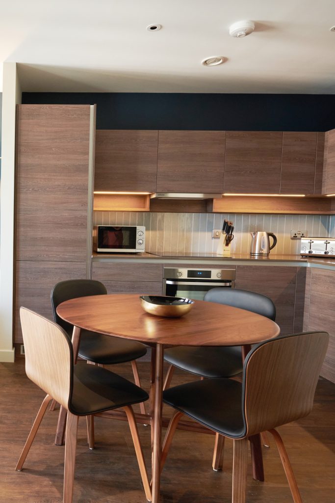 Modern kitchen with wood cabinetry, round dining table, and black-accented chairs.