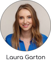 A woman with light brown, wavy hair wears a blue shirt and a delicate necklace.