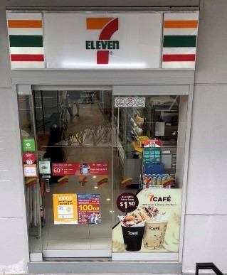 Entrance of a 7-Eleven store with promotional posters and glass doors displaying interior items.