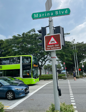 A street sign for Marina Blvd with a caution sign and vehicles at a pedestrian crossing.