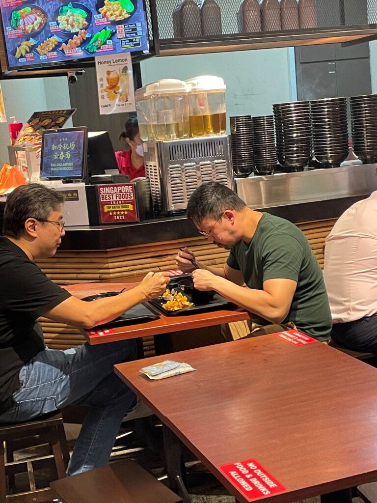 Two individuals dine at a casual eatery with menu displays and beverage dispensers in the background.
