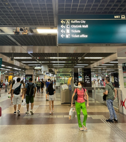 Commuters navigate a busy MRT station with directional signs and ticketing facilities visible.
