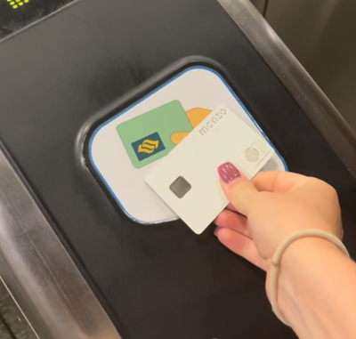 A hand holds two cards over a contactless payment terminal, preparing for a transaction.