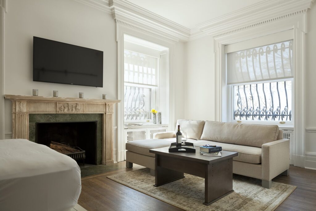 Elegant living room with a beige sofa, fireplace, mounted TV, and large windows with iron grilles.