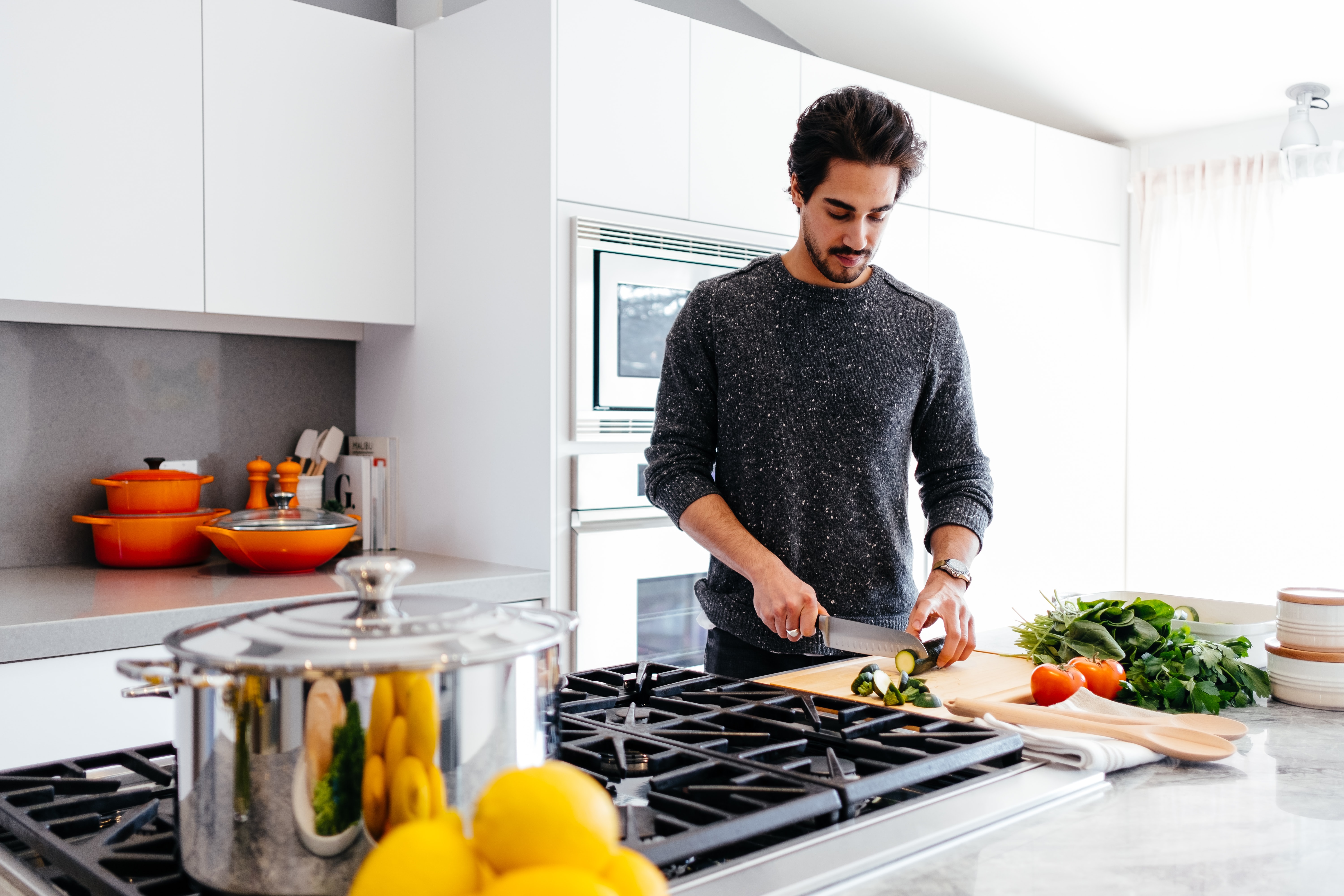 A person chops vegetables in a modern kitchen with white cabinets and stainless steel appliances.