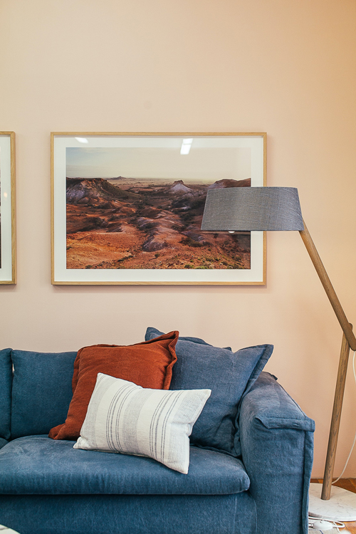 A cozy living space with a blue sofa, accent pillows, a floor lamp, and framed landscape artwork.