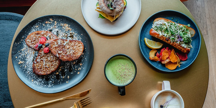 A stylish brunch spread featuring French toast, a sandwich, a loaded hot dog, and vibrant drinks.