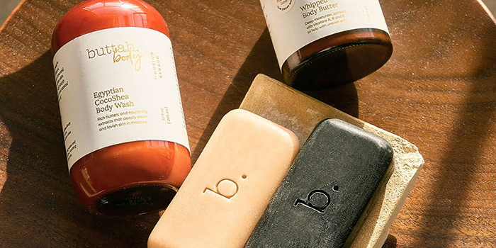 Skincare products, including body wash, body butter, and soap bars, displayed on a wooden surface.