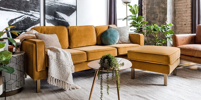A mustard-yellow sofa with a matching ottoman in a modern living room with plants and decor.