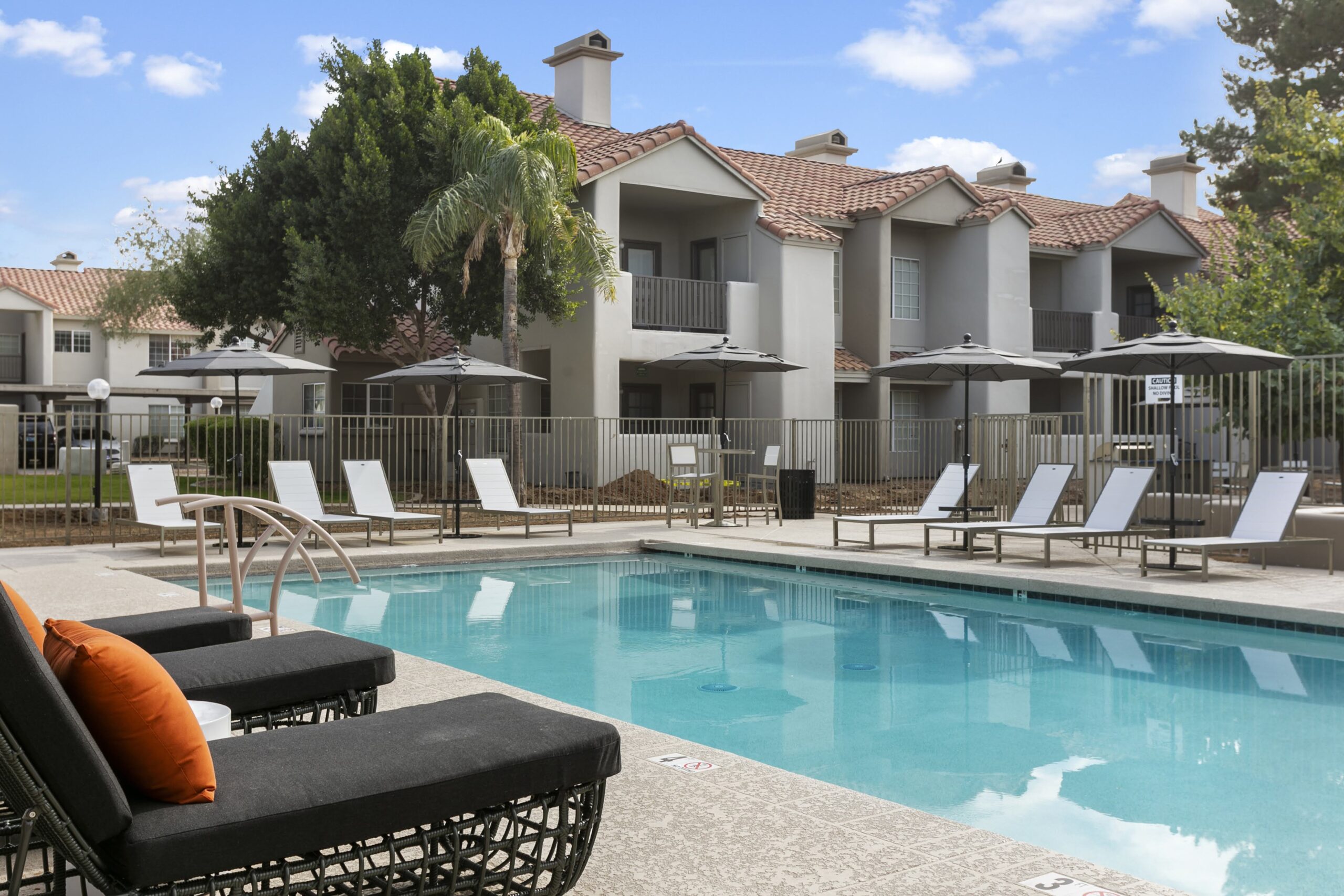 A modern pool area with lounge chairs, umbrellas, and adjacent Mediterranean-style apartments.