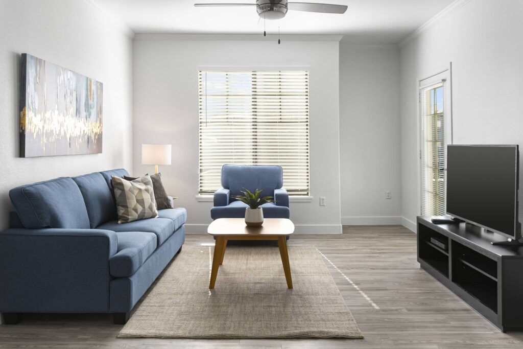 Modern living room with blue furniture, neutral decor, and natural light from large windows.