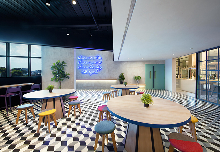 Modern cafeteria with geometric flooring, colorful stools, and neon wall art.