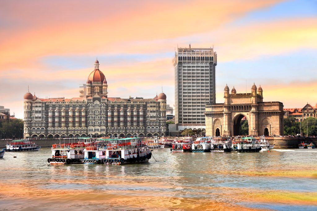 Gateway of India and Taj Mahal Palace Hotel in Mumbai, with boats on the Arabian Sea at sunset.