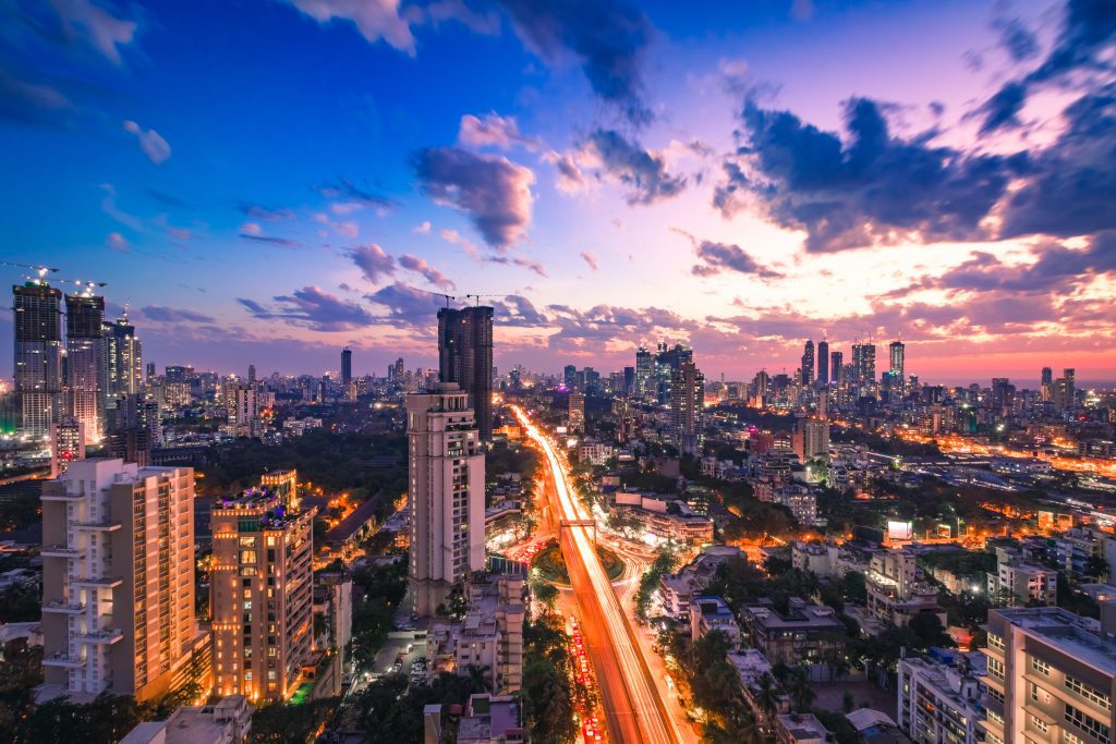 A vibrant cityscape at dusk with illuminated buildings and streaks of traffic lights.