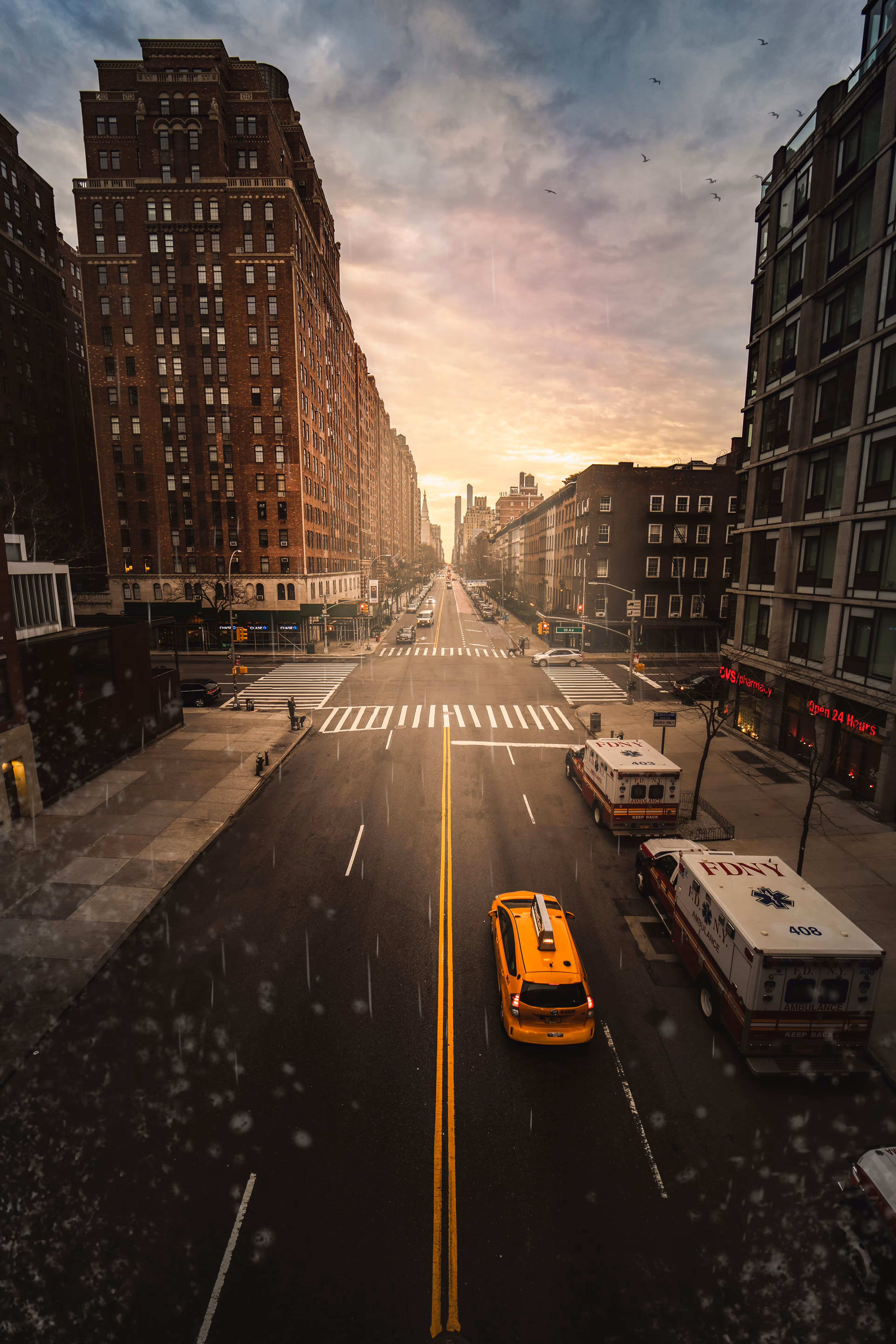 Stadtstraße bei Sonnenuntergang mit gelbem Taxi und geparkten FDNY-Ambulanzfahrzeugen in New York.