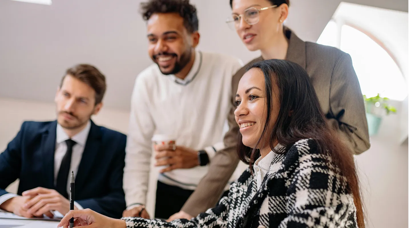 Group of four diverse colleagues smiling and collaborating in a bright office setting.