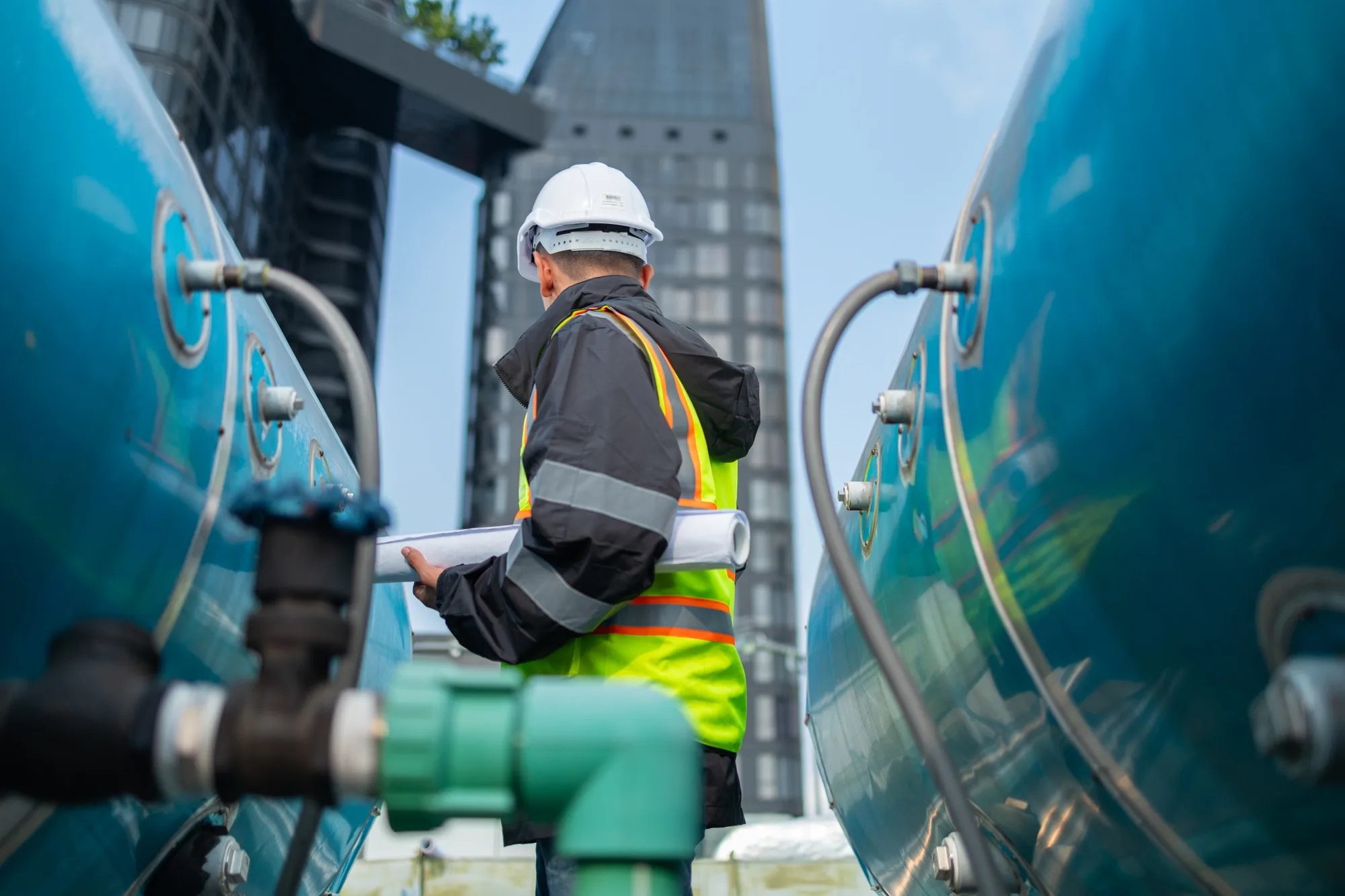 Engineer inspects water heater pump system and hot water tank on industrial roofEngineer inspects water heater pump system and hot water tank on industrial roof