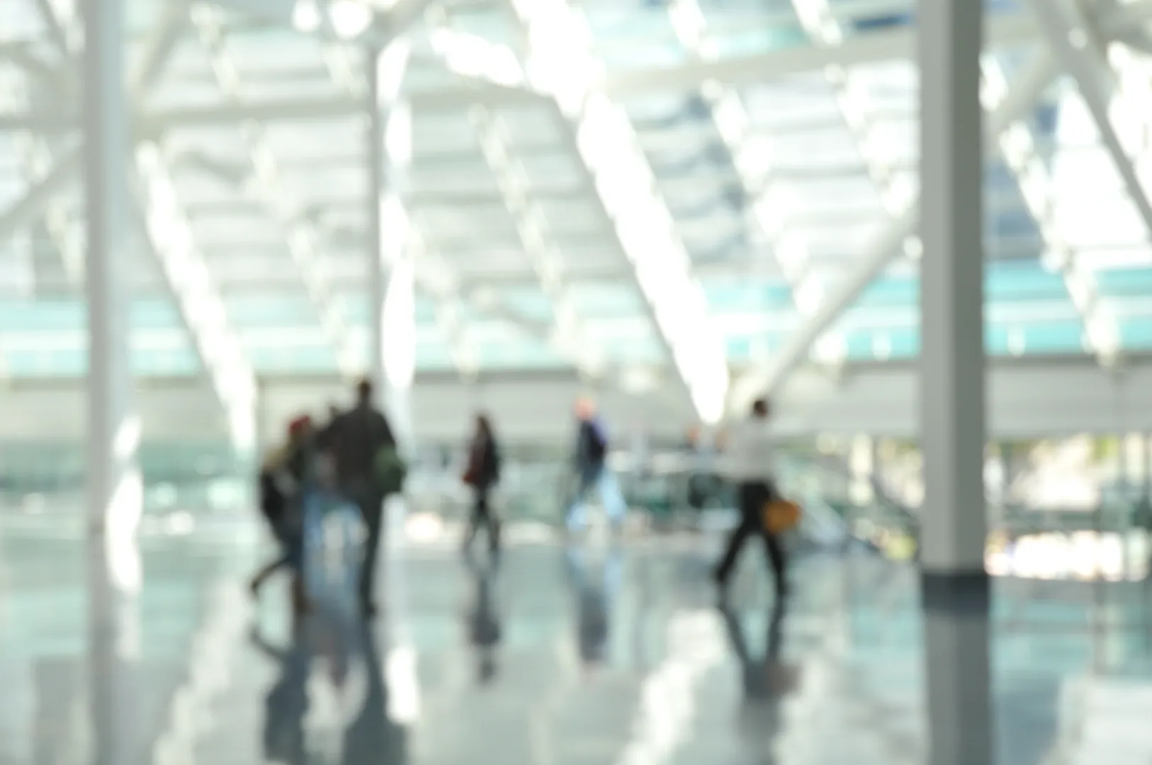 Blurred image of people walking inside a modern building with large glass windows and reflective floors.