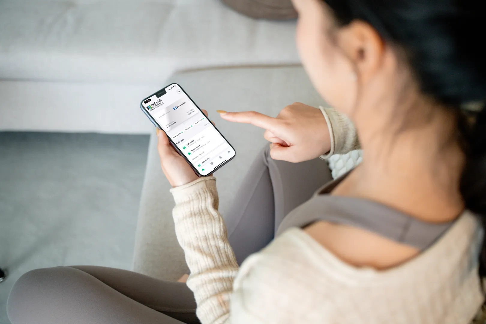 Person holding and pointing at a smartphone displaying the Wells Insurance app interface.