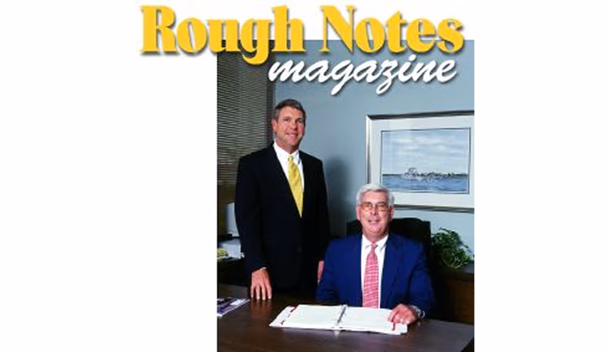 Cover of Rough Notes magazine featuring two men in business attire, one standing and one seated at a desk with an open binder.