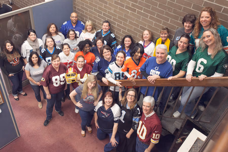 Group of women and one man wearing various NFL jerseys posing on a staircase and indoors.