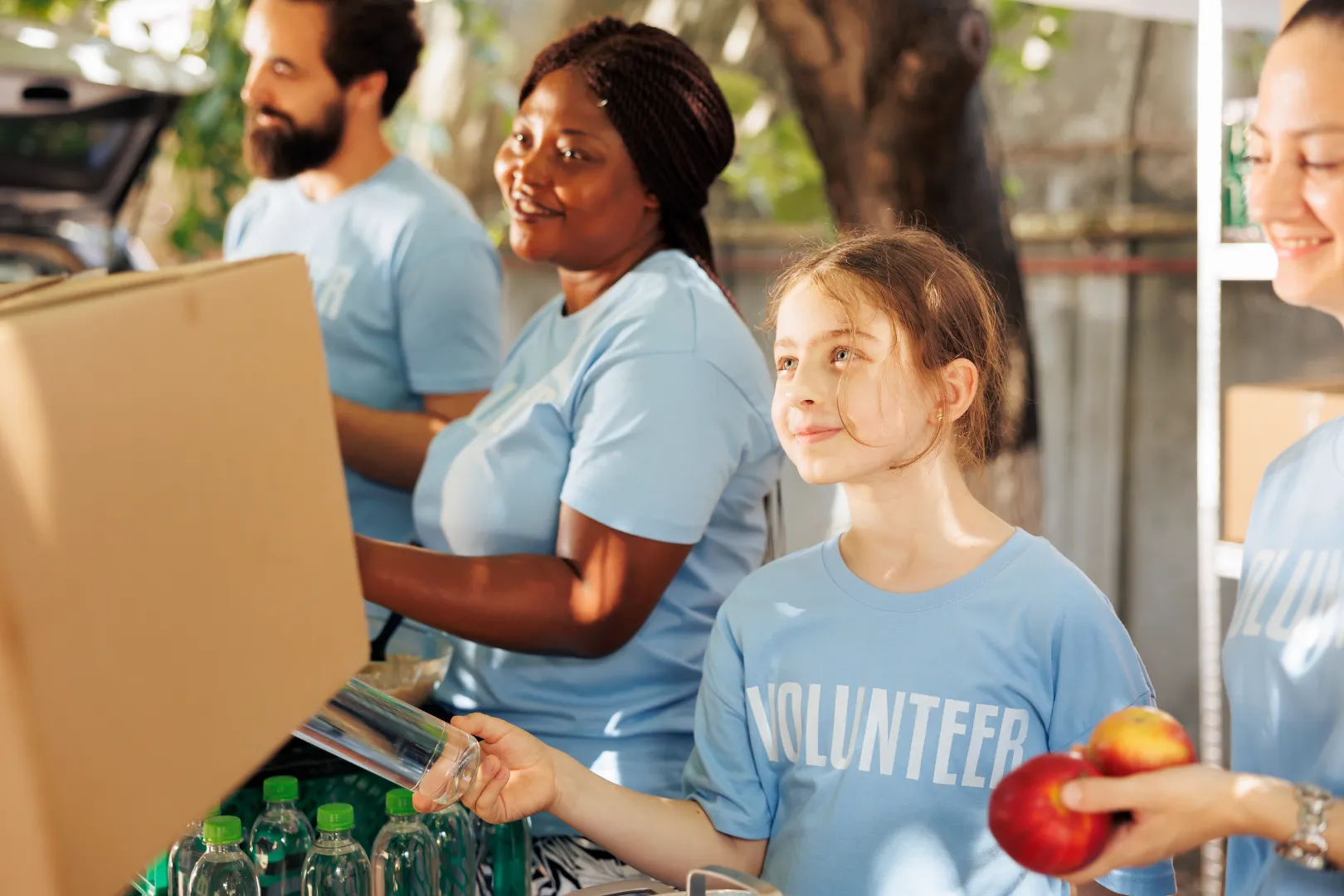 A group of volunteers in blue shirts packing boxes with food and bottled water.