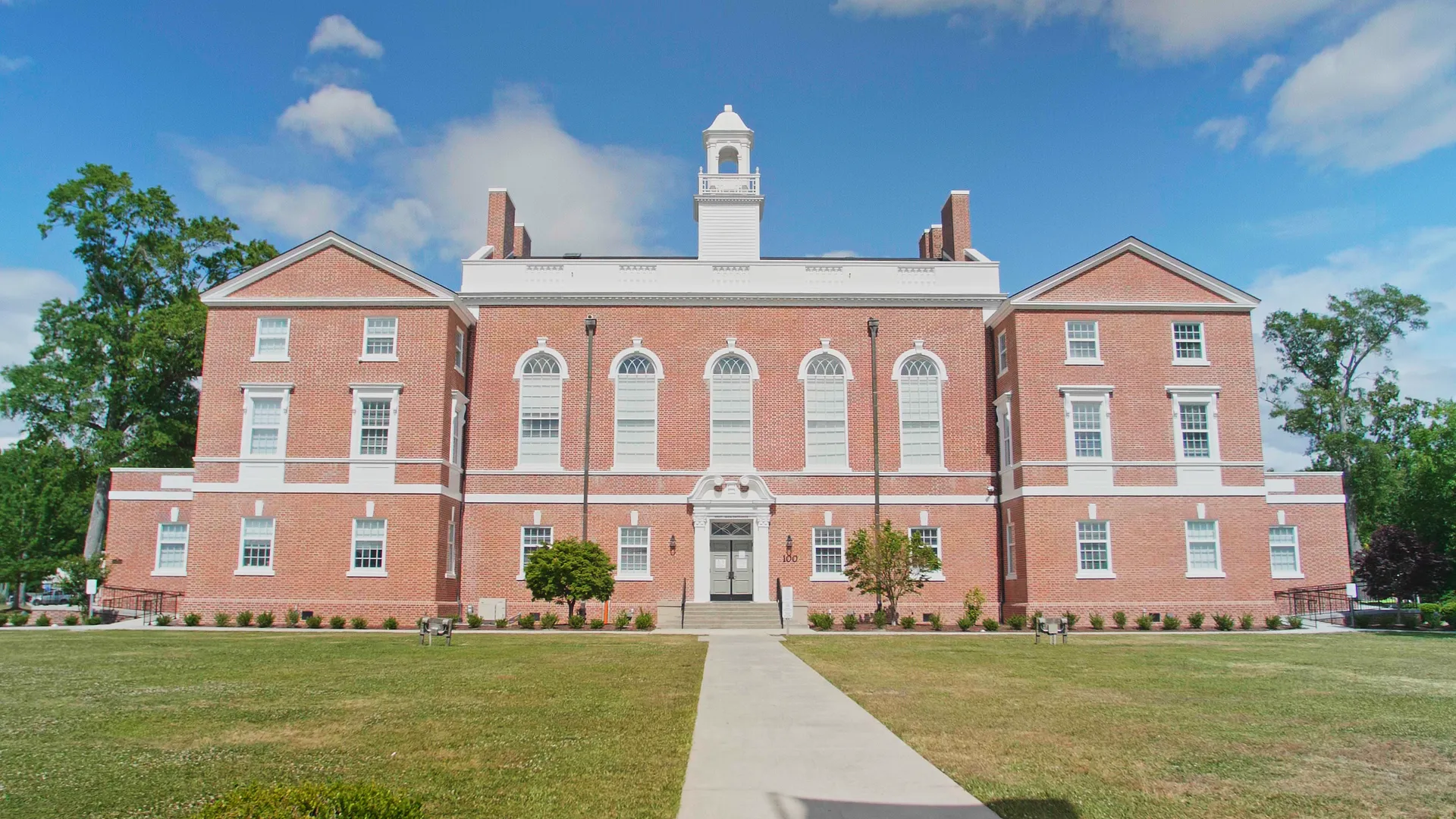 Symmetrical red brick building with white trim and a central cupola under a blue sky.