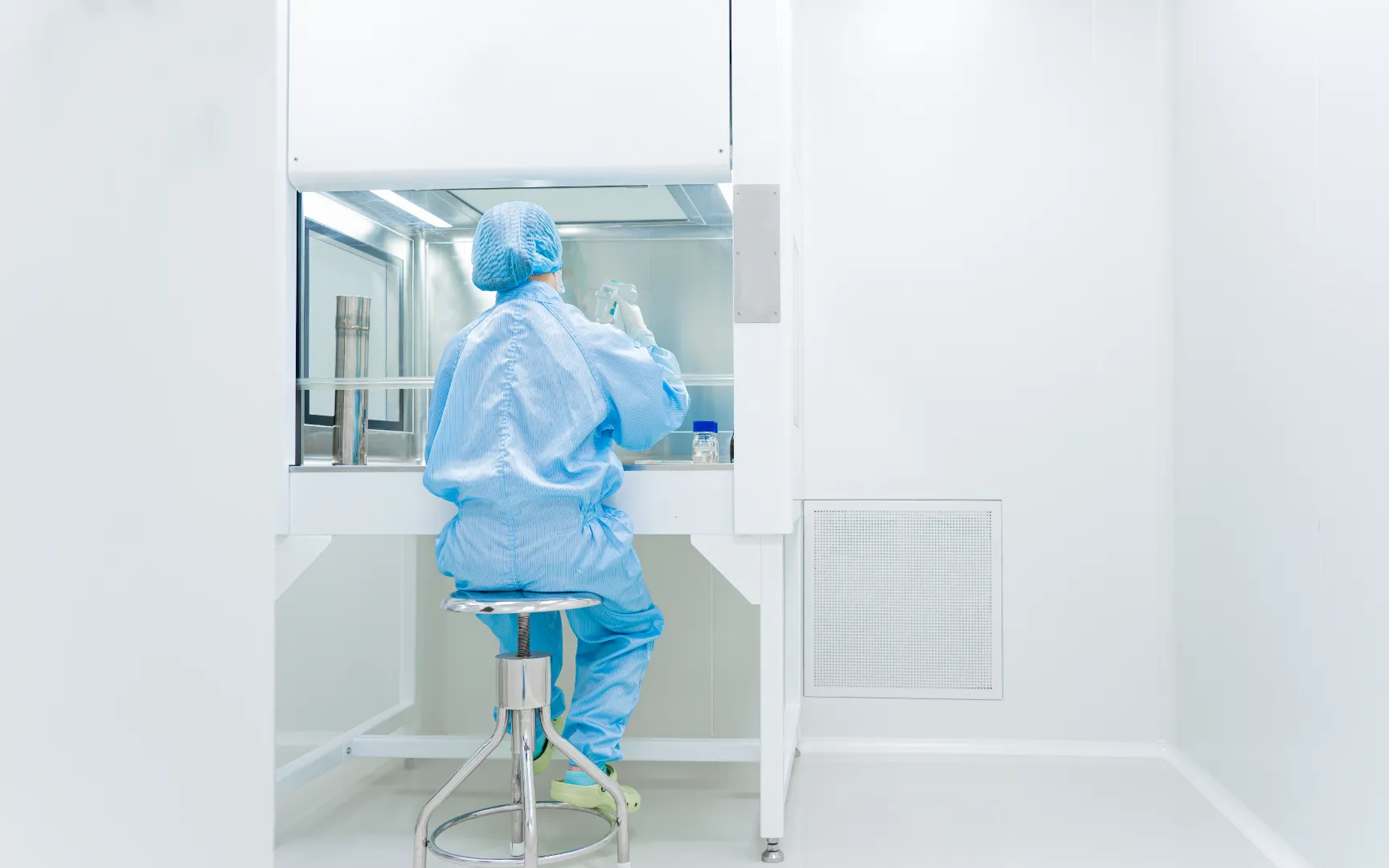 Scientist in blue protective suit working at a laboratory clean bench handling a bottle.