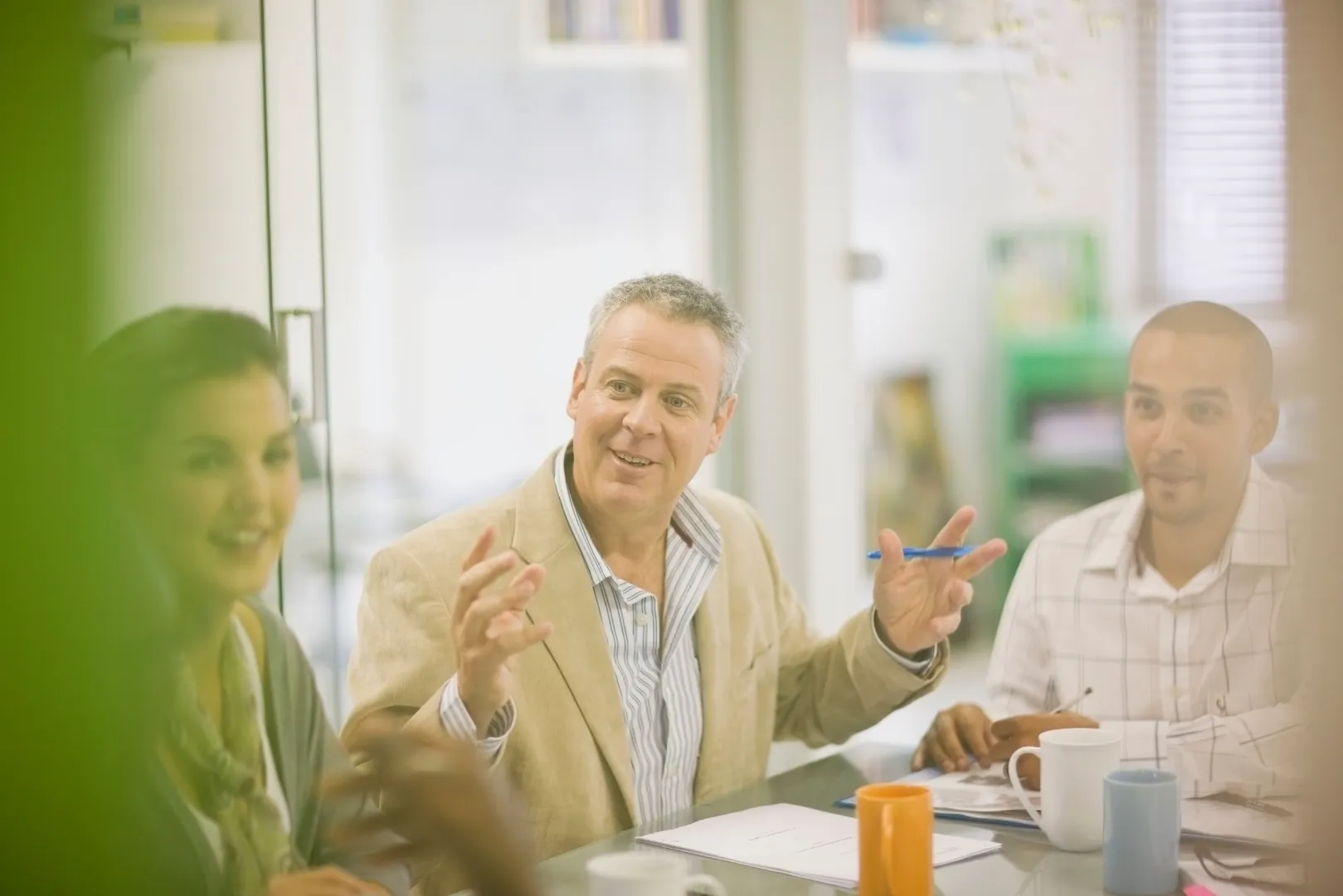 Three colleagues having a discussion around a table with documents and coffee mugs.
