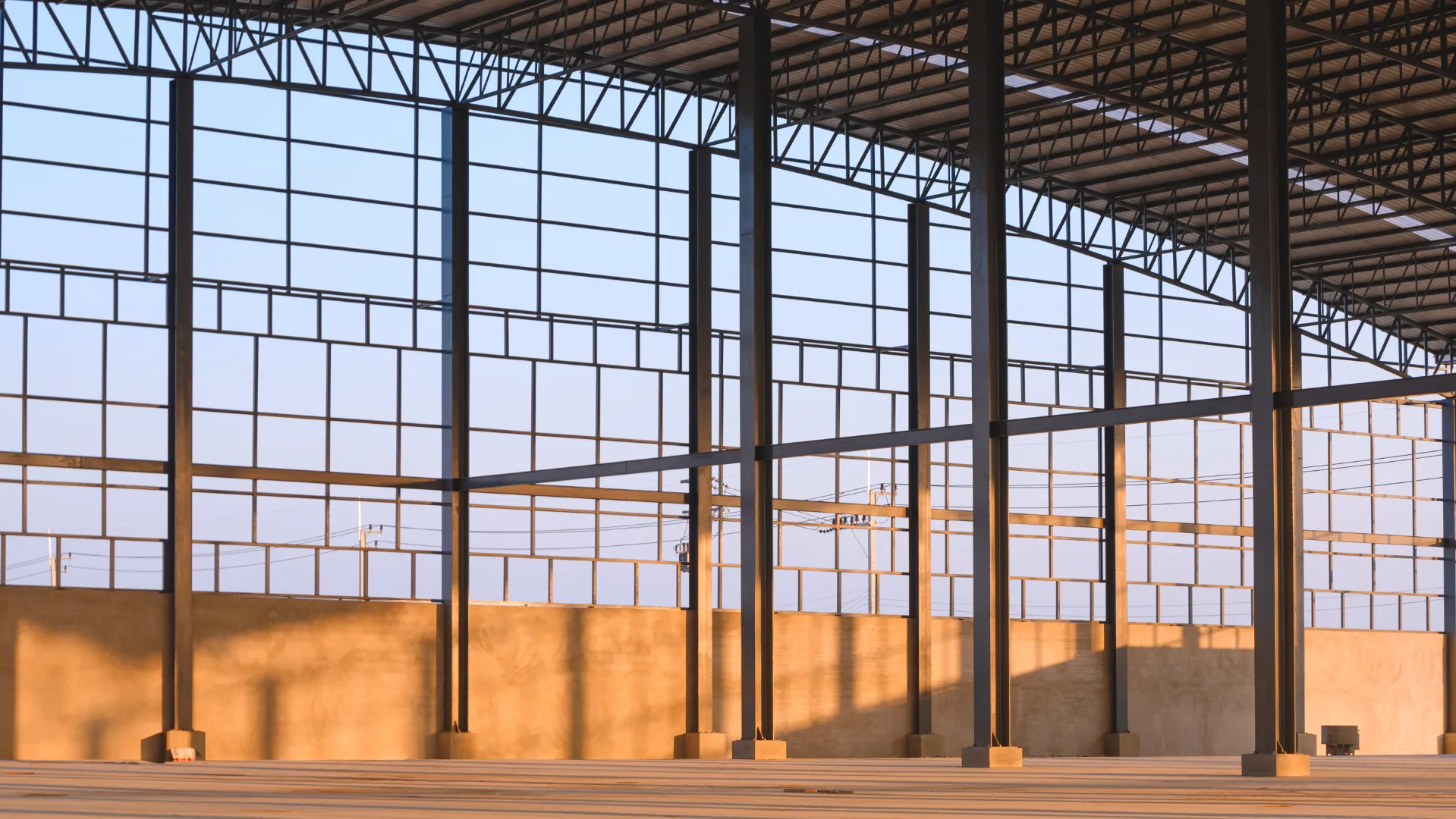 Interior of a spacious empty industrial warehouse with large windows and steel support beams.