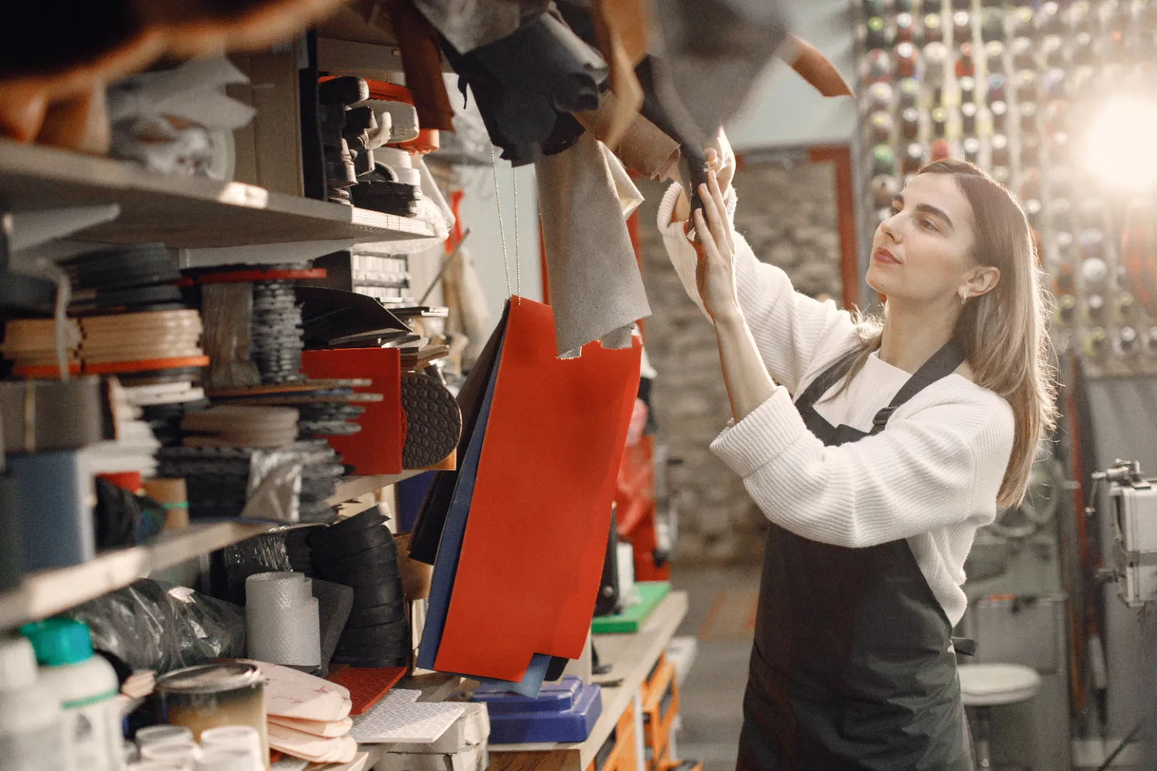 Woman in a workshop wearing an apron inspecting hanging leather or fabric samples.