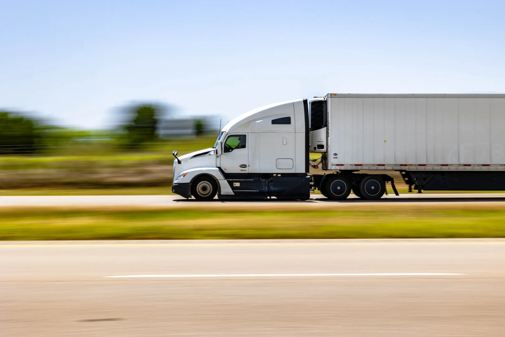 White semi-truck with trailer driving fast on highway with blurred background.