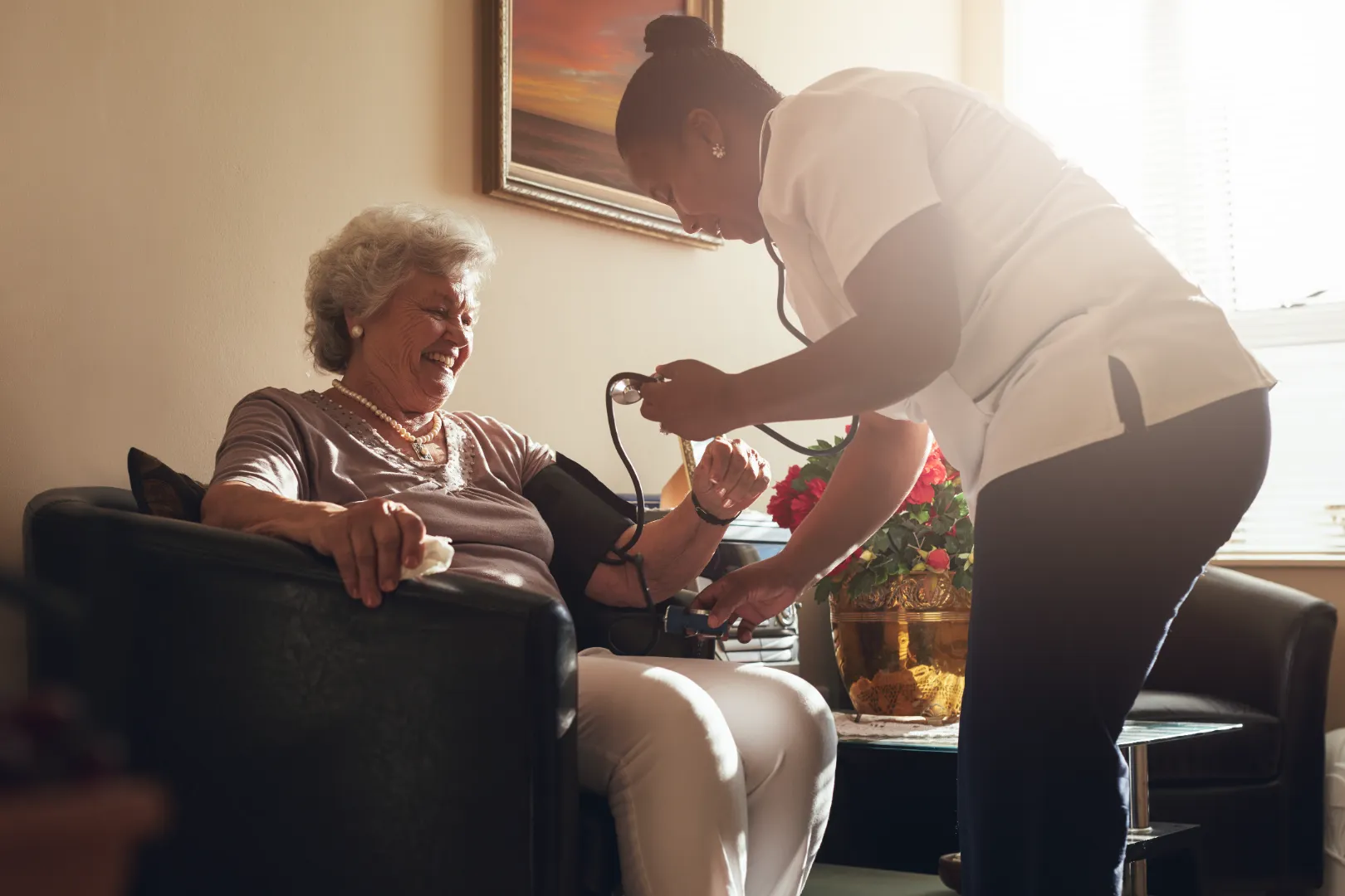 Nurse measuring elderly woman's blood pressure in a cozy living room with warm lighting.